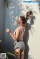 A woman standing in front of a wall with her hair in a ponytail.