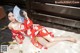 A woman in a red kimono laying on the sand with a fan.