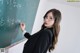 A woman wearing glasses writing on a blackboard.