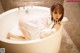 A woman in a white shirt is sitting in a bathtub.